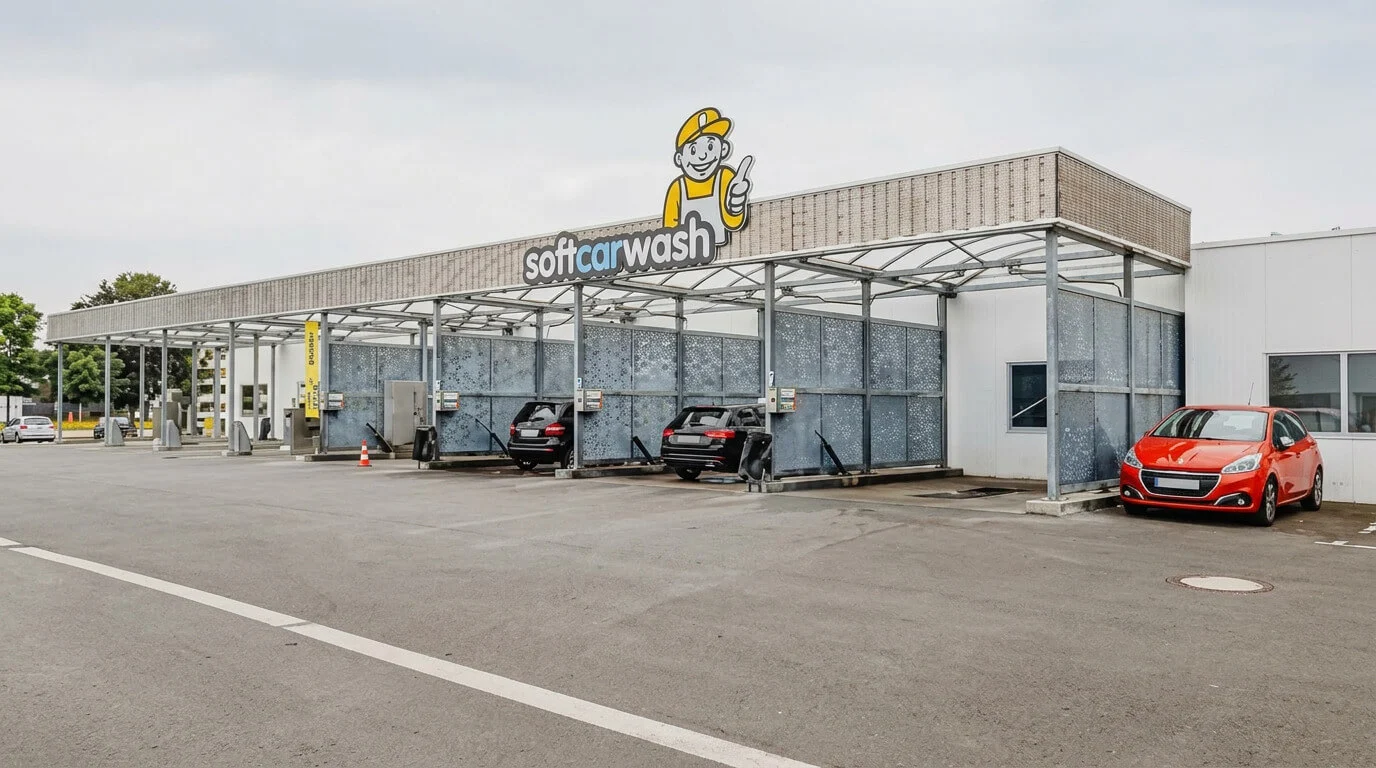 Selbstbedienungs-Autowaschanlage im Freien mit mehreren Autos und einem Schild mit einer Comic-Figur darüber. Selbstbedienungs-Autowaschanlage im Freien mit mehreren Autos und einem Schild mit einer Comic-Figur darüber.