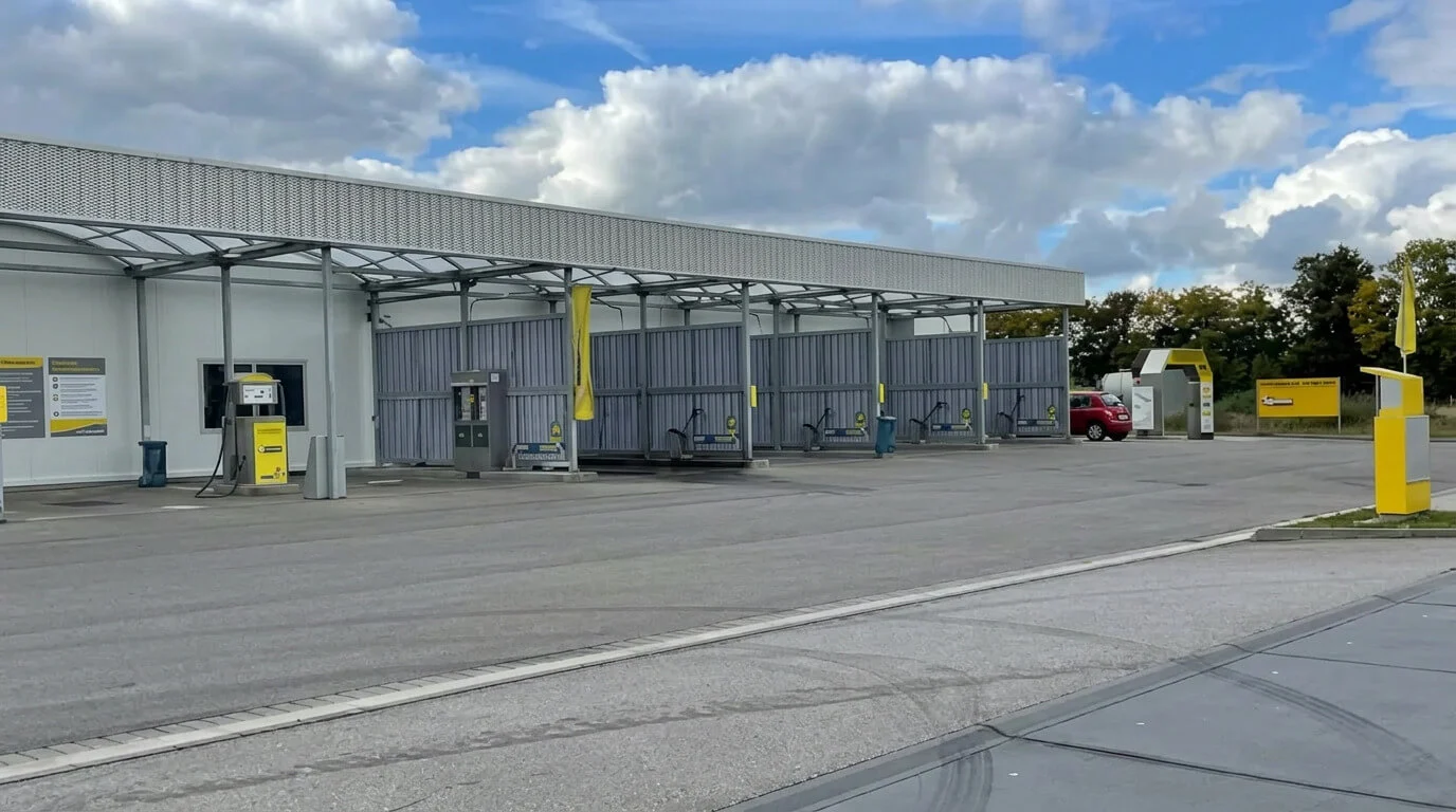 Selbstbedienungs-Autowaschanlage mit Waschplätzen, einem roten Auto und einem teilweise bewölkten Himmel. Selbstbedienungs-Autowaschanlage mit Waschplätzen, einem roten Auto und einem teilweise bewölkten Himmel.